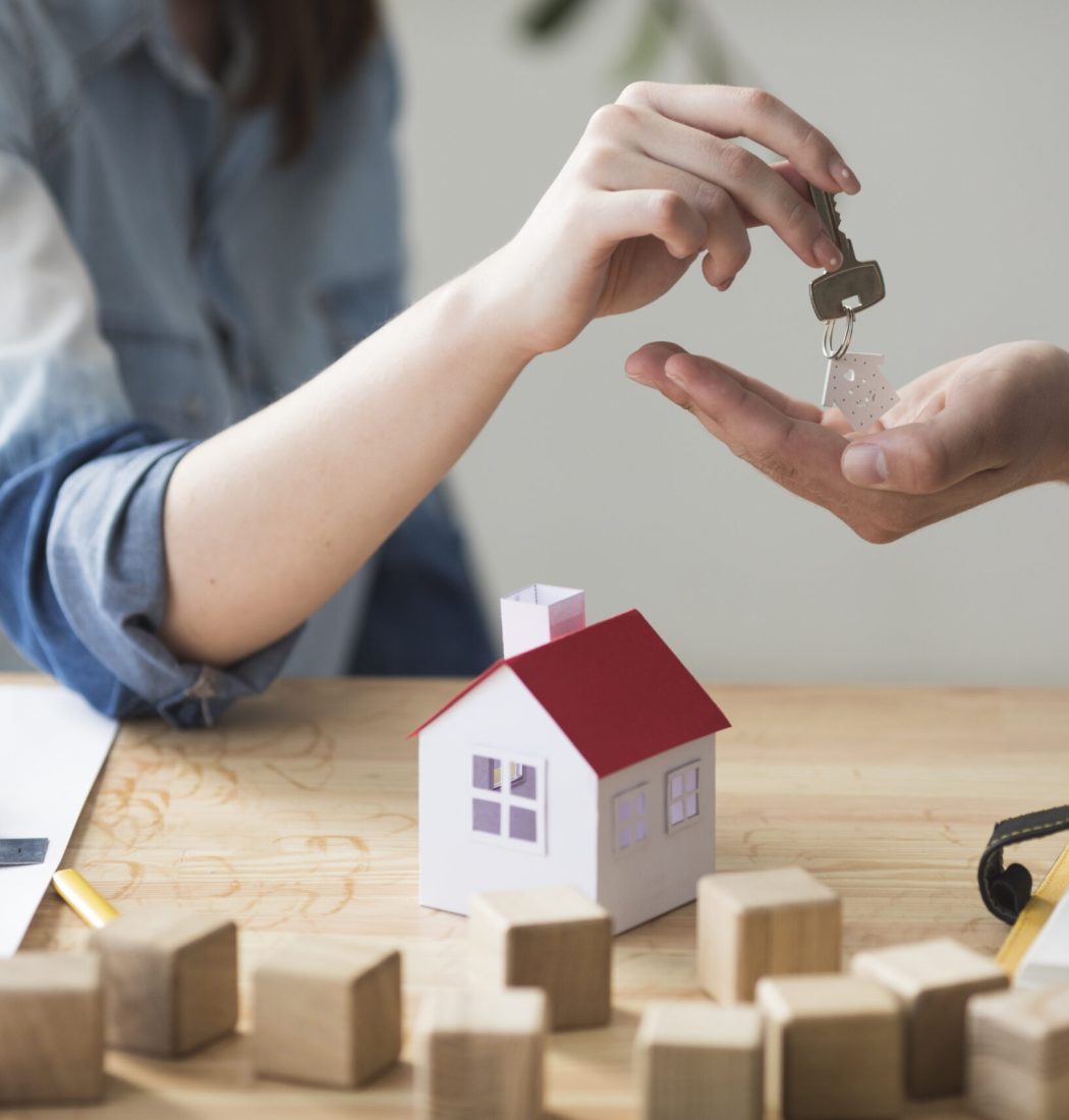 close-up-woman-s-hand-giving-house-key-man-wooden-table